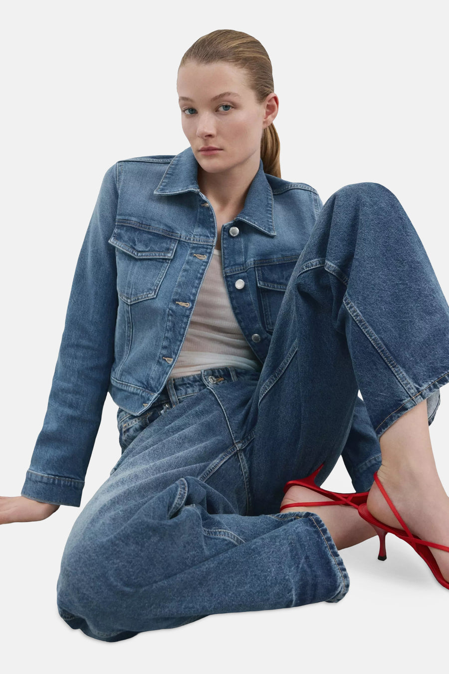 Blauwe spijkerjas van MANGO met zilverkleurige knopen, gedragen met een witte top, een wijde jeans en rode sandalen met hak.
