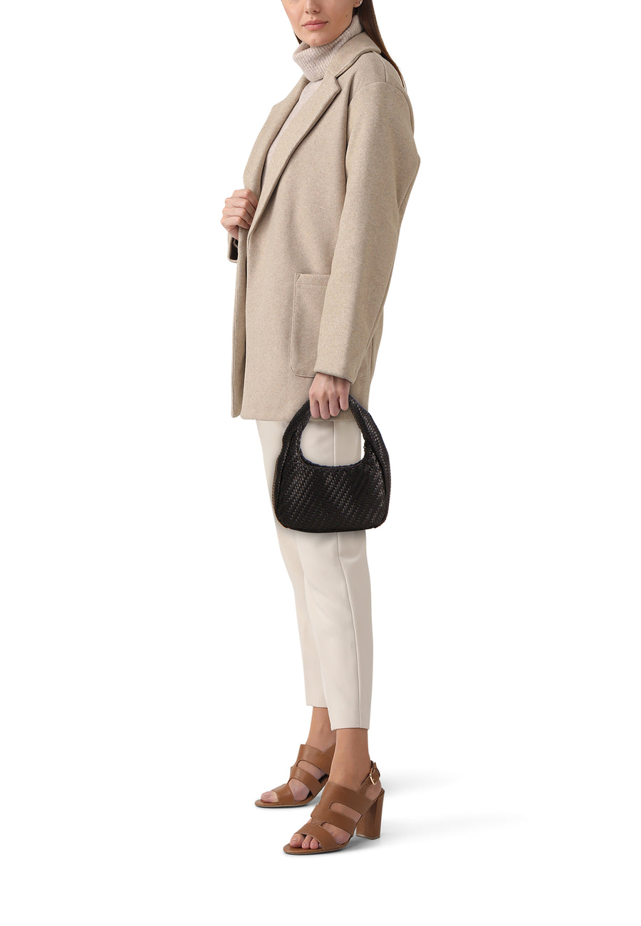 Sac à bandoulière noir de MANGO, petit, tressé, tenu à la main par un modèle en manteau beige et pantalon crème.