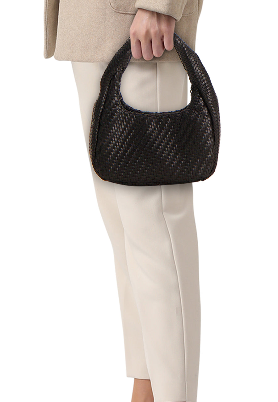 Sac à bandoulière noir de MANGO tressé, tenu par une main, avec un manteau beige et un pantalon clair.