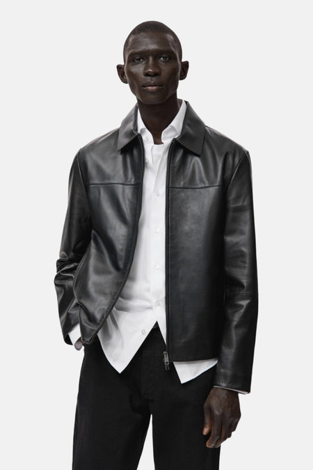 Veste courte noire de MANGO, portée avec une chemise blanche et un pantalon noir.
