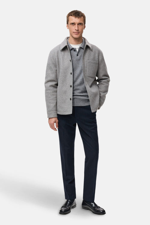 Veste courte grise par MANGO, avec boutons, portée sur un pull gris à col polo et un pantalon bleu marine.