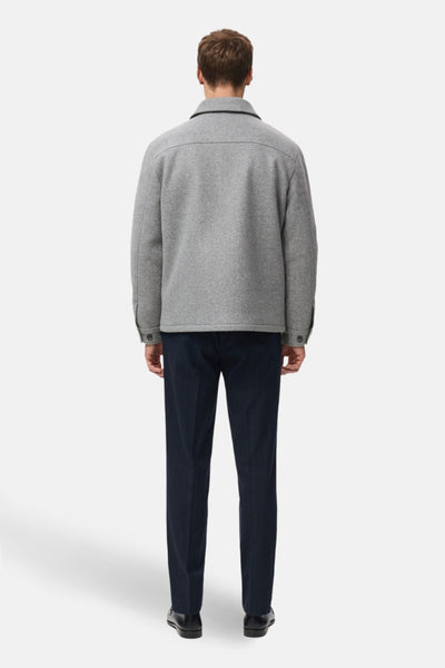 Veste courte grise par MANGO, coupe droite, avec col classique et poches poitrine, portée avec un pantalon bleu marine.
