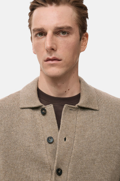 Beige vest van MANGO, in breisel met donkere knopen, gedragen over een bruin T-shirt.