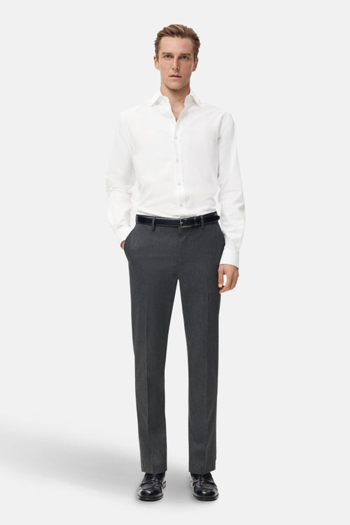 Chemise blanche à manches longues de MANGO, portée avec pantalon de costume gris et ceinture noire.