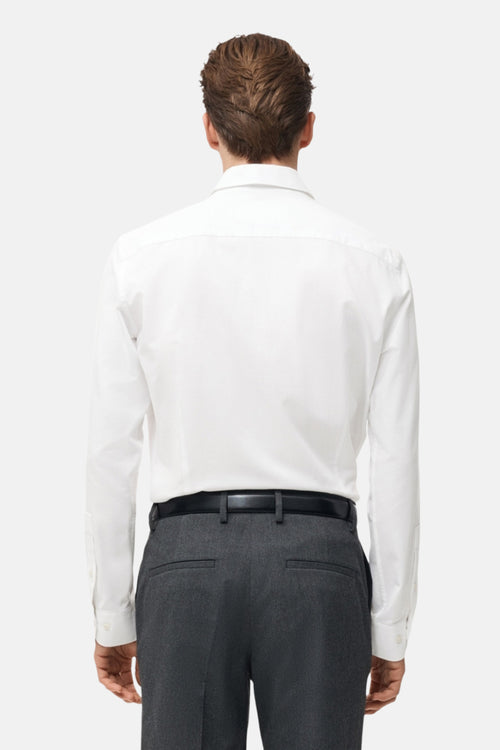 Chemise blanche à manches longues de MANGO, portée avec un pantalon gris et une ceinture noire, vue de dos.
