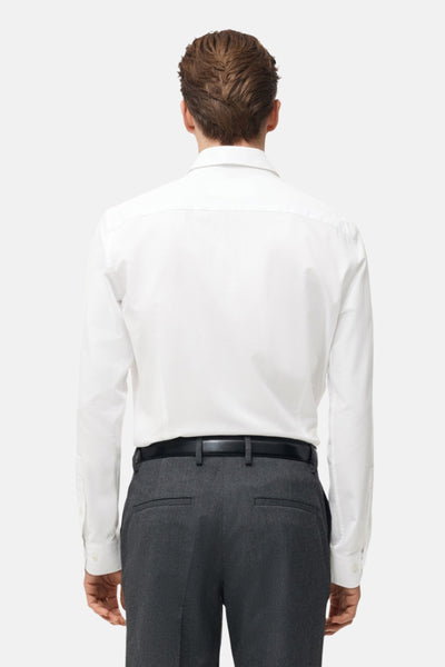 Chemise blanche à manches longues de MANGO, portée avec un pantalon gris et une ceinture noire, vue de dos.
