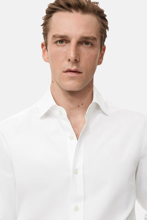Chemise à manches longues blanche de MANGO, portée avec un col ouvert et des boutons visibles.