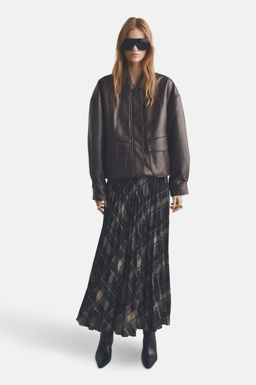 Jupe longue à carreaux multicolores de MANGO, portée avec une veste en cuir marron et des bottines noires.
