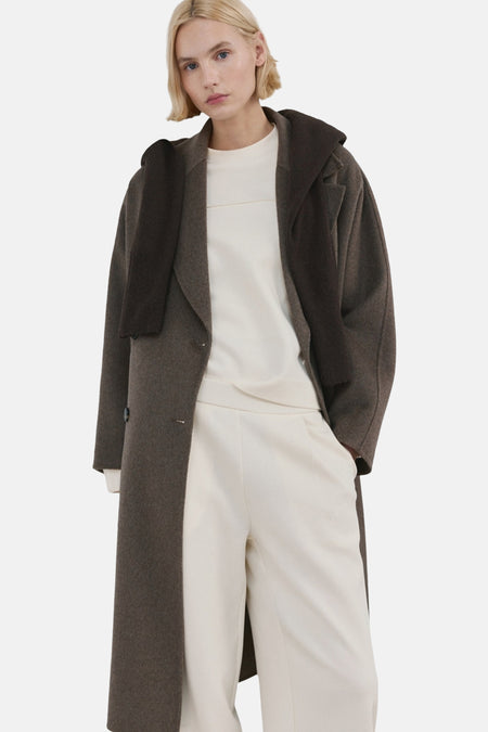 Sweat col rond beige de MANGO, porté avec un manteau long marron et un pantalon ample blanc.