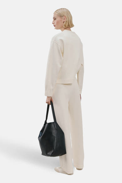 Beige ronde hals sweatshirt van MANGO, gedragen met een crèmekleurige broek en een zwarte handtas.