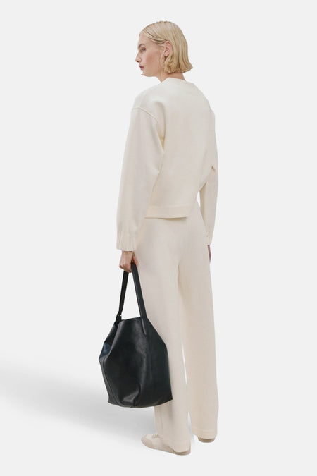 Sweat col rond beige de MANGO, porté avec un pantalon crème et un sac à main noir.