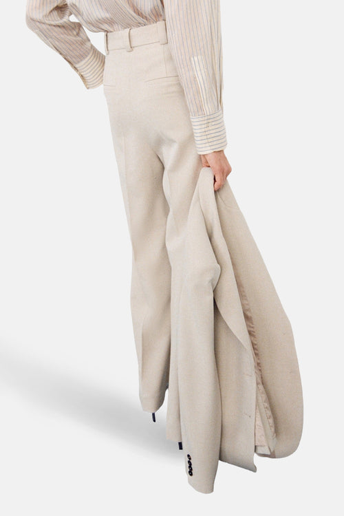 Pantalon beige de MANGO avec une texture légèrement chinée, porté avec une chemise rayée.