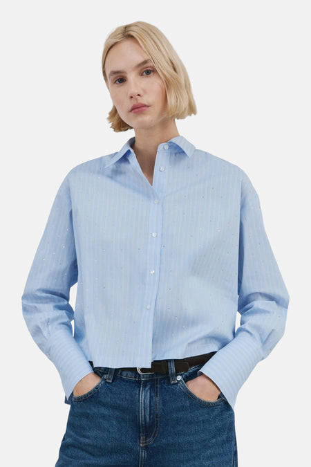 Chemise à manches longues bleue rayée de MANGO, ornée de petits points brillants, portée avec un jean.
