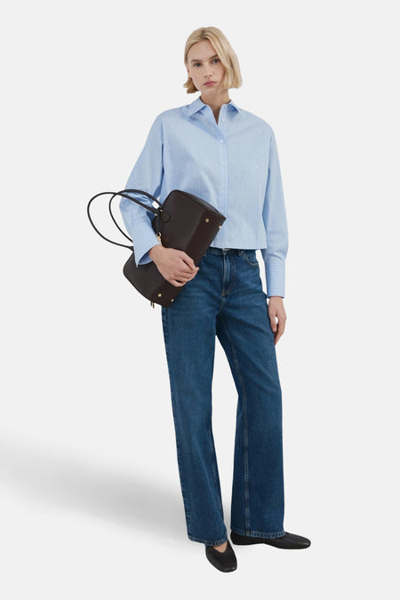 Chemise à manches longues bleue à rayures, par MANGO, portée avec un jean bleu et des chaussures noires.
