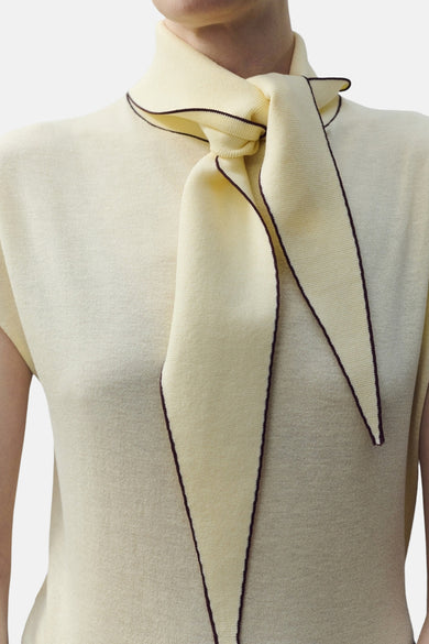 Chemisier sans manches jaune by MANGO, avec col montant noué et détails de bordure contrastée.
