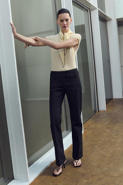 Chemisier jaune sans manches de MANGO, porté avec un pantalon noir et des sandales à talons aiguilles.
