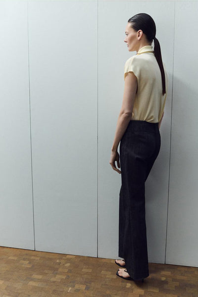 Gele mouwloze blouse van MANGO, gedragen met een donkere broek en hakken, zijwaarts gezien.