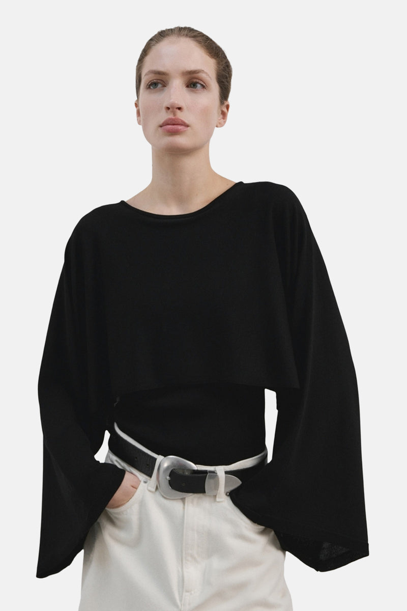 Pull à col rond noir de MANGO, porté sur un haut noir avec un jean blanc et une ceinture argentée.