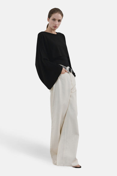 Pull à col rond noir de MANGO, à manches larges et amples, porté avec un pantalon large écru et une ceinture argentée.