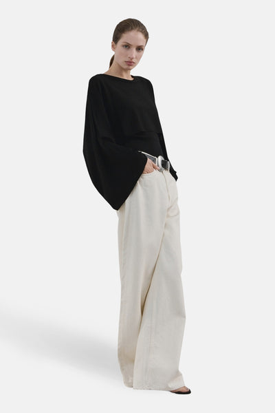 Pull à col rond noir de MANGO, à manches larges et amples, porté avec un pantalon large écru et une ceinture argentée.