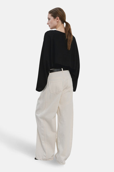 Pull à col rond noir de MANGO, porté avec un pantalon taille haute ample couleur crème.
