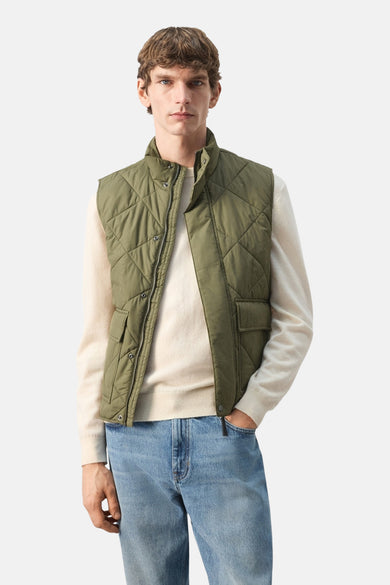 Bodywarmer kaki by MANGO, avec motif matelassé en losanges, porté sur un pull beige avec un jean bleu.
