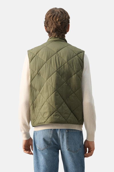 Bodywarmer kaki par MANGO, à motif losanges matelassé, porté sur un pull beige et un jean bleu, vue de dos.

