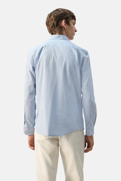Chemise à manches longues bleue de MANGO, motif à carreaux discrets, portée avec un pantalon clair, vue de dos.