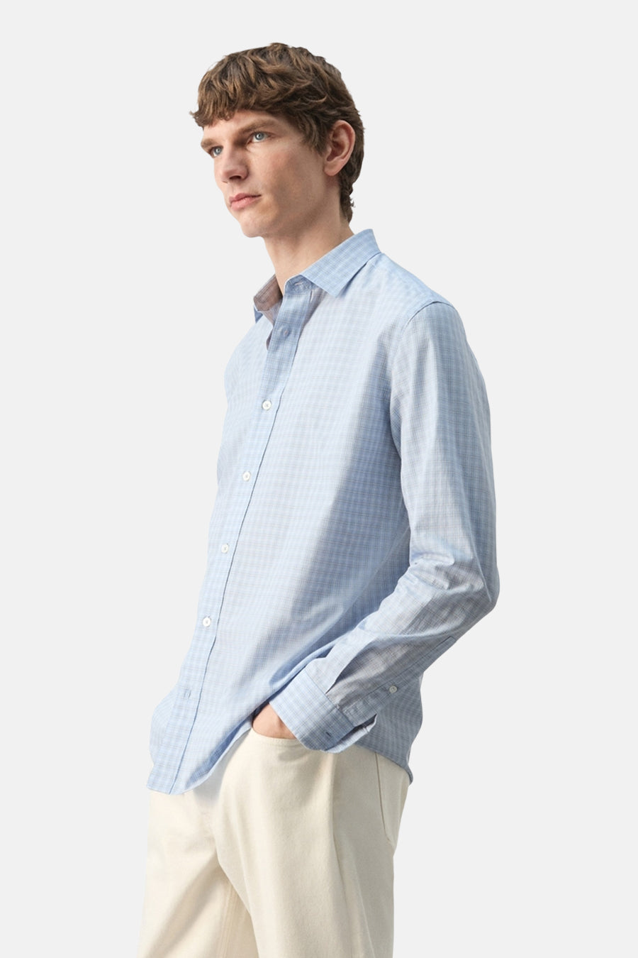Blauw overhemd met lange mouwen van MANGO, met subtiele ruit, gedragen met een lichte broek, zijwaarts gezien.