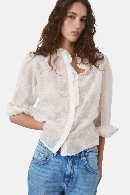 Chemisier beige à manches longues de MANGO, avec motif floral et détail de volants, porté avec un jean bleu.