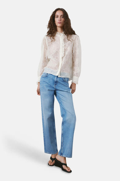 Beige blouse met lange mouwen van MANGO, met delicate bloemendetails en een ruchekraag, gedragen met een wijde blauwe jeans.