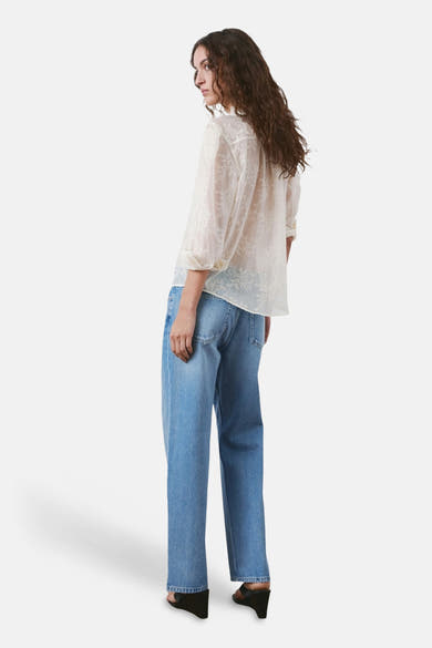 Chemisier beige à manches longues de MANGO, avec un motif floral délicat et une coupe décontractée, porté avec un jean bleu.
