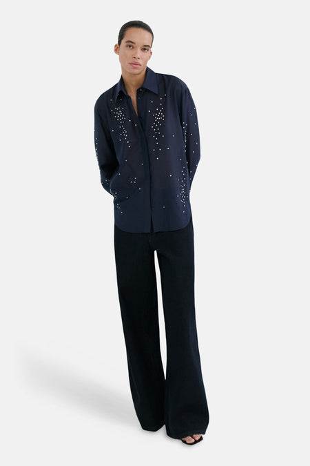 Chemise bleue à manches longues par MANGO, ornée de motifs de petits points blancs, portée avec un pantalon foncé évasé.