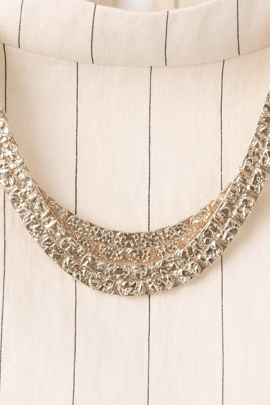 Blouse écrue van MANGO, à rayures verticales noires, ornée d'un collier décoratif argenté texturé.
