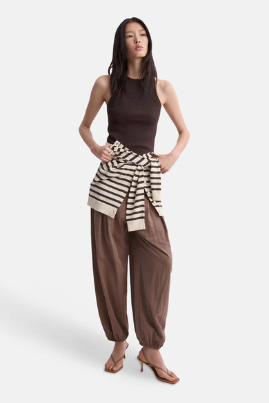 Top sans manches côtelé brun de MANGO, porté par une mannequin avec un pantalon ample marron et un pull rayé noué.