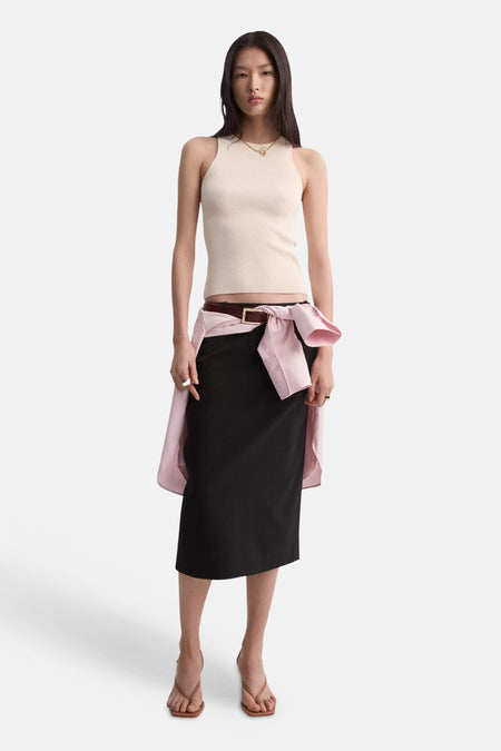 Top sans manches beige côtelé de MANGO, porté avec une jupe noire et une chemise rose nouée.