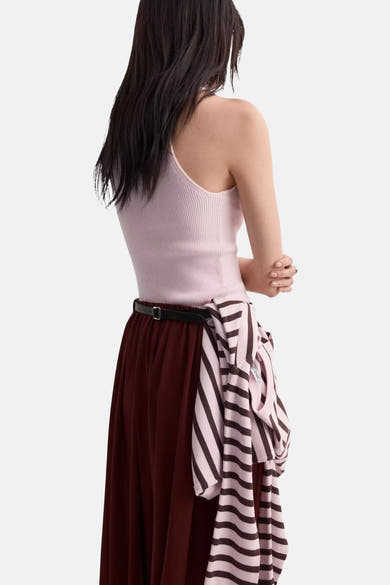 Top sans manches rose pâle côtelé de MANGO, porté de dos avec un pull rayé rose et marron noué à la taille et une jupe bordeaux.