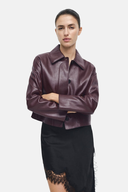 Veste courte bordeaux en cuir de MANGO, portée avec une jupe noire à bordure en dentelle.