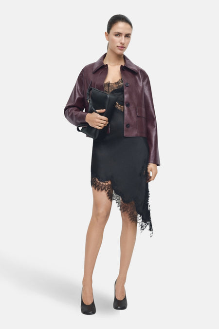 Veste courte bordeaux de MANGO, portée sur une robe noire en dentelle, avec un sac noir assorti et des chaussures noires.
