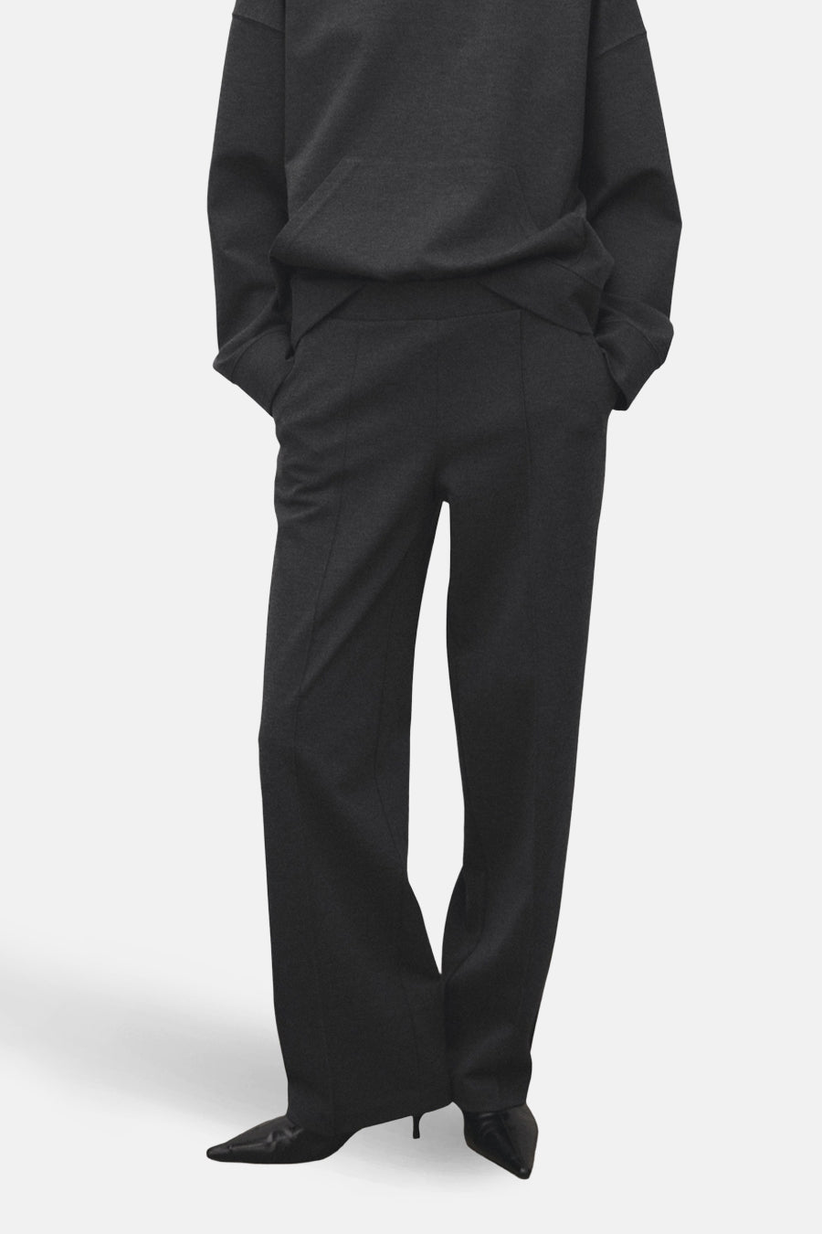 Pantalon gris de MANGO, avec une coupe droite et des plis verticaux, associé à un sweat-shirt foncé.
