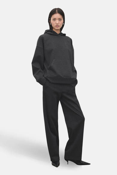 Pantalon gris de MANGO, avec coupe ample et taille haute, porté avec un sweat à capuche assorti et des escarpins noirs.