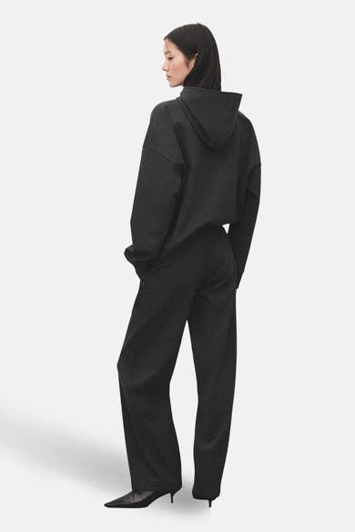 Pantalon gris de MANGO, coupe droite, porté avec un sweat à capuche et des escarpins noirs.