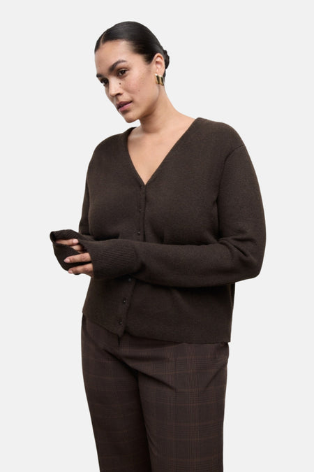 Gilet marron van MANGO, porté avec un pantalon à carreaux marron et des boucles d'oreilles dorées.