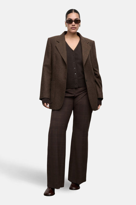 Gilet brun, par MANGO, porté avec un blazer marron texturé, un pantalon à carreaux et des lunettes de soleil.