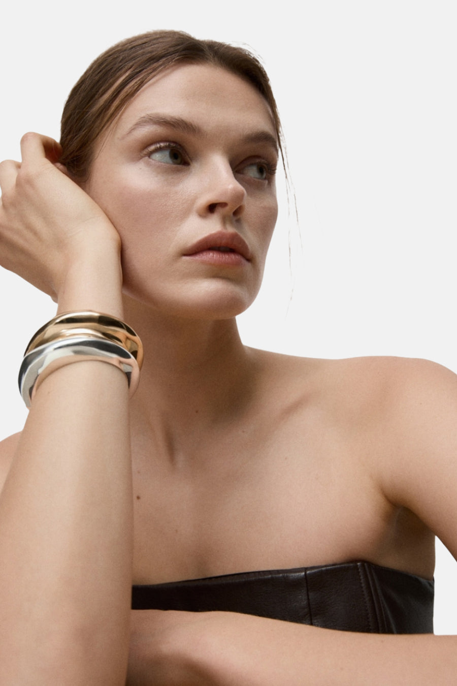 Bracelet doré par MANGO, porté au poignet d’une femme portant un bustier en cuir.