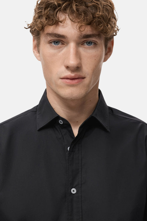 Chemise à manches longues noire de MANGO, avec une patte de boutonnage sur le devant.
