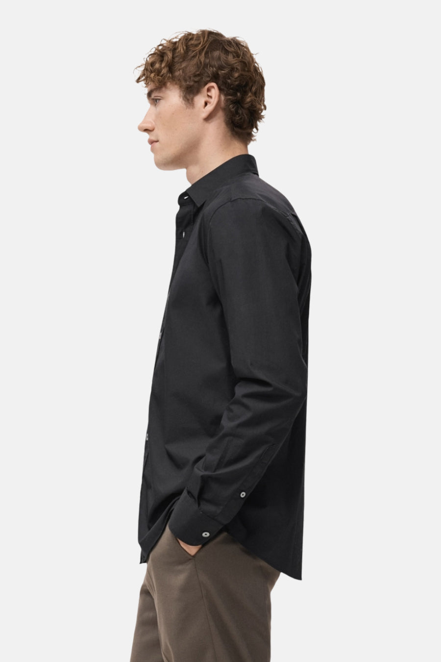 Zwart overhemd met lange mouwen van MANGO, zijprofiel, gedragen met een bruine broek.