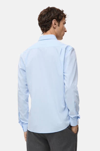 Chemise à manches longues bleue de MANGO, vue de dos, portée avec un pantalon gris foncé.