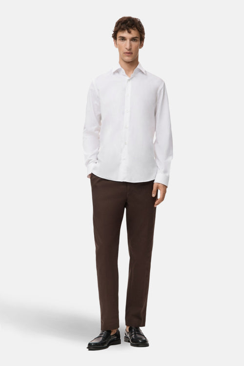 Chemise blanche à manches longues de MANGO, portée avec un pantalon marron et des chaussures noires.