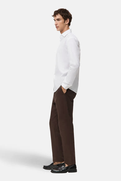 Wit overhemd met lange mouwen van MANGO, gedragen met een bruine broek en zwarte loafers, zijwaarts gezien.